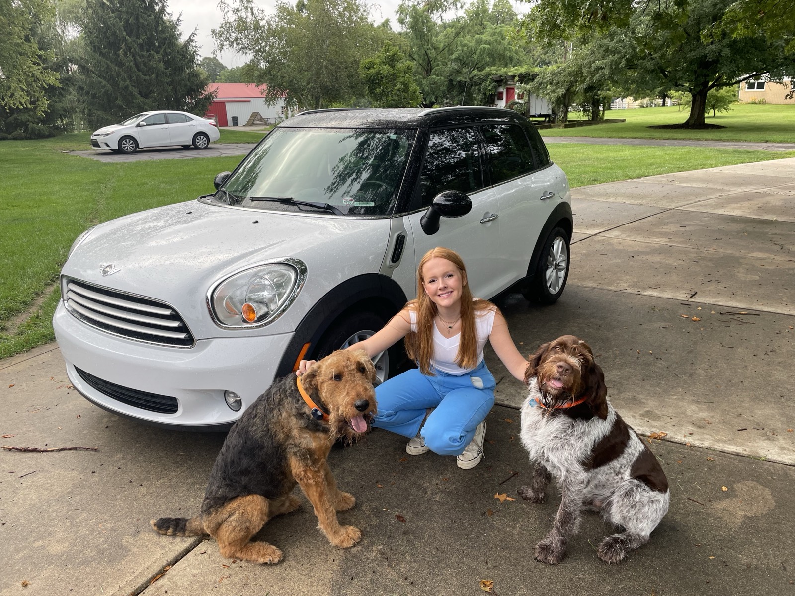 Teagan kneeling between two happy dogs in front of her car